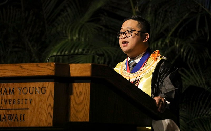 Young man in graduation robes speaking at a podium