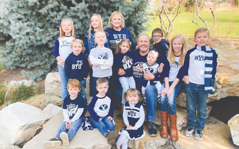 two adults with 12 grandchildren outdoors wearing Brigham Young University shirts