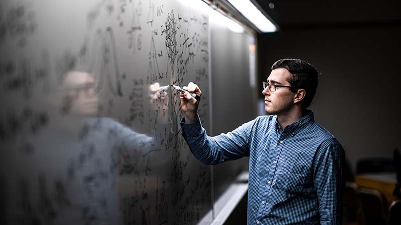 BYU math student works on an equation on a whiteboard.