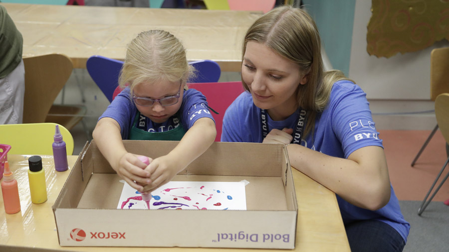 A young woman helping a small girl with paints while doing a craft