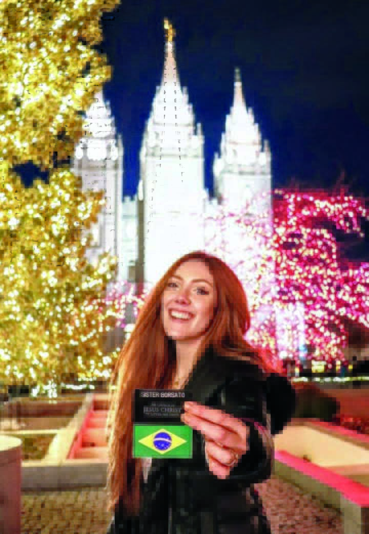 woman holding her missionary name tag in front of the Salt Lake Temple at Christmas time