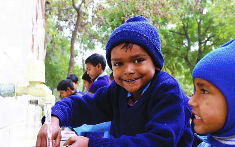 Photo of boys outside filling cups with clean water that runs from white faucets.