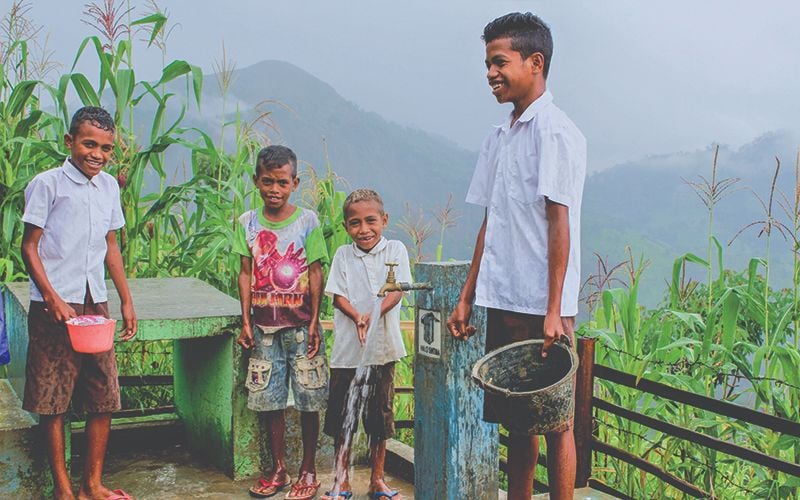 Four boys standing outside filling containers with clean water running from a faucet.