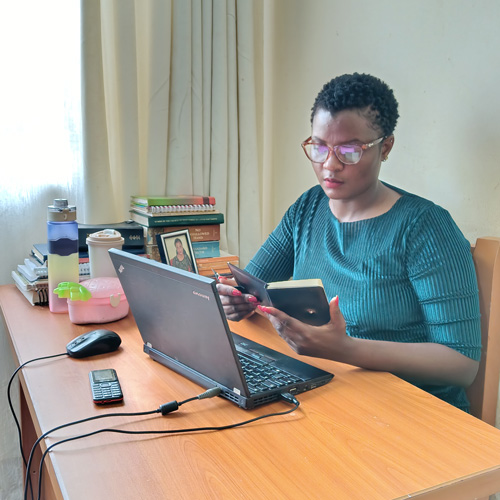 African woman sitting at a desk in her home with a laptop and an notebook.