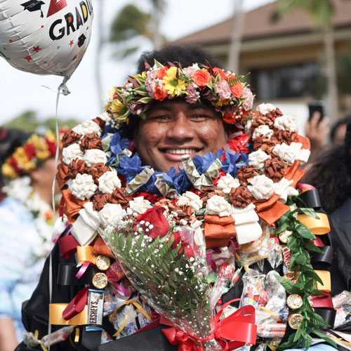 A man wearing a graduation gown and several leis stacked up to his chin.