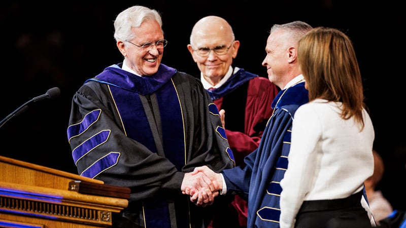 BYU President Shane Reese shaking hands with Elder D. Todd Christofferson with Elder Dallin H. Oaks smiling in background