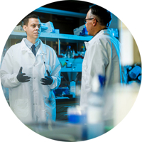 Male BYU student in a lab coat talking with a BYU professor in a lab
