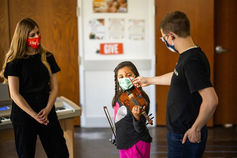 Two young adults and a young girl holding a violin.