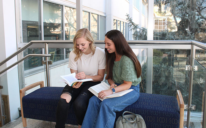 two lady BYU students sitting on a bench reading from books