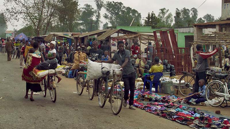 A street market in Malawi with people carrying goods on bicycles.