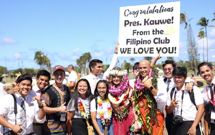 A group of students standing with President and Sister Kauwe and holding a sign that says “We love you.”