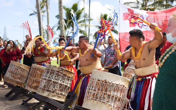 Men in traditional Tongan clothing enthusiastically playing drums.
