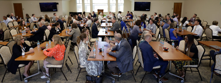 A large group of tables with PLC members meeting and talking with BYU students