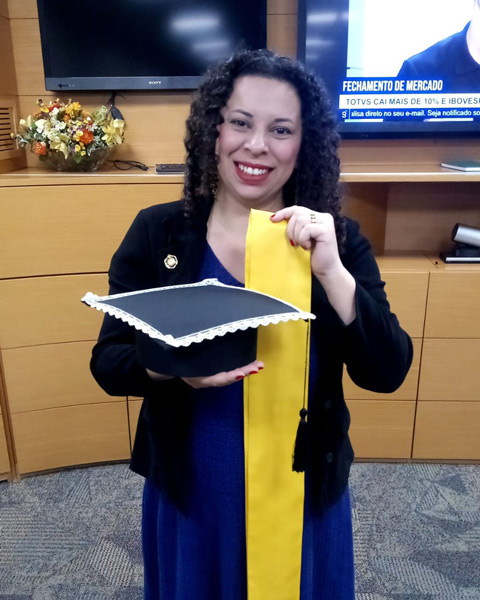 Young Latina holding a graduation cap and yellow graduation sash.