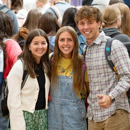 Three BYU-Idaho students smiling in a large group of students