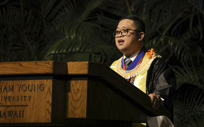 Young man in graduation robes speaking at a podium
