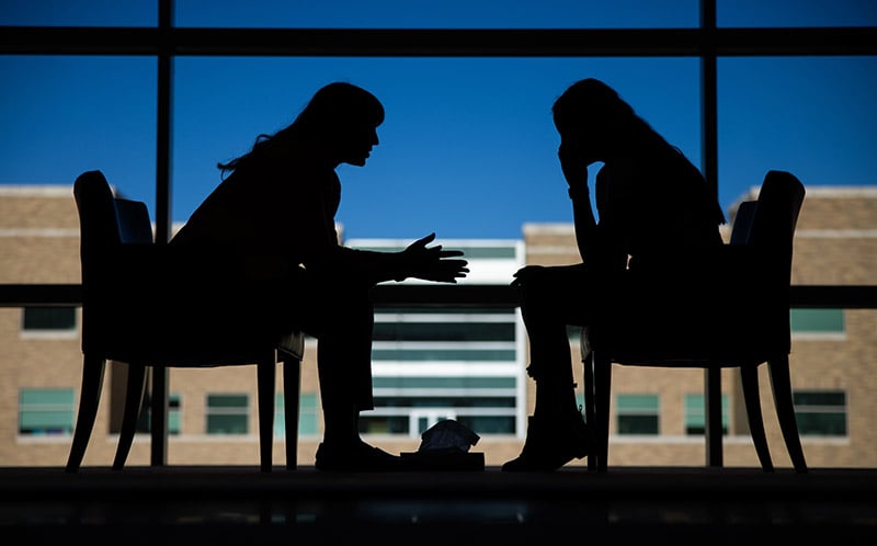 Silhouette of two people having a conversation in front of a window.