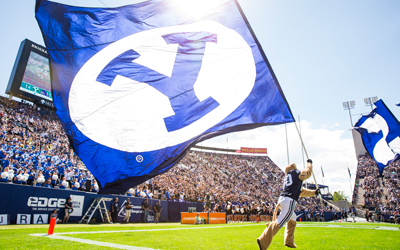 Cosmo the Cougar running with a large BYU flag at a BYU football game.