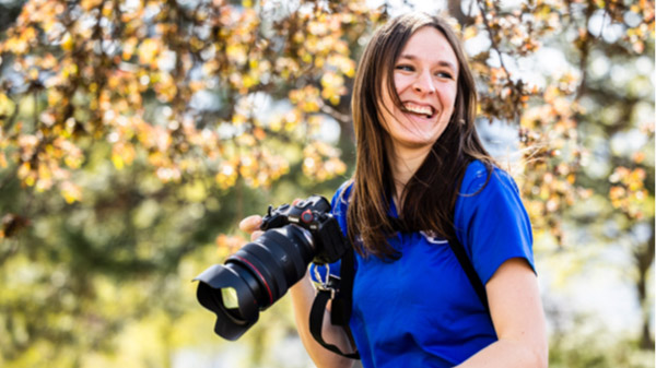Brooklyn Jarvis Kelson wearing a blue shirt holding a camera and smiling.