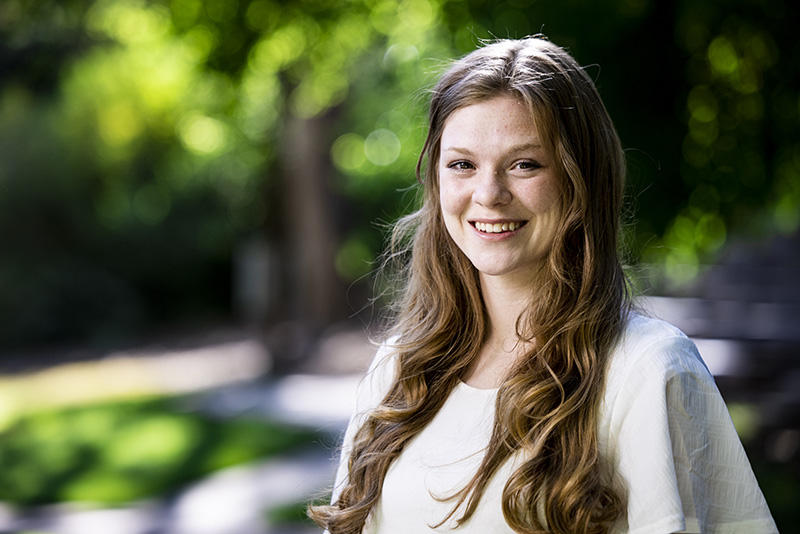 A student with long hair wearing a white dress among trees