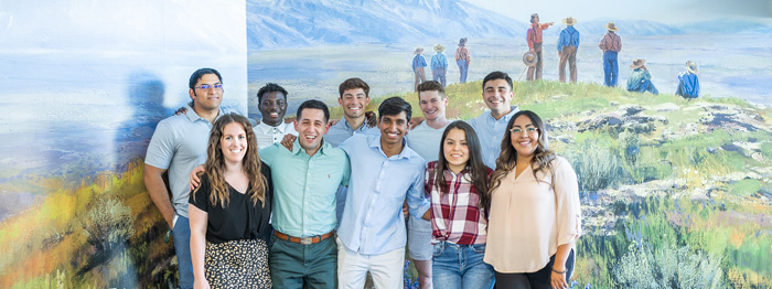 Group of Ensign College students in front of a pioneer mural.