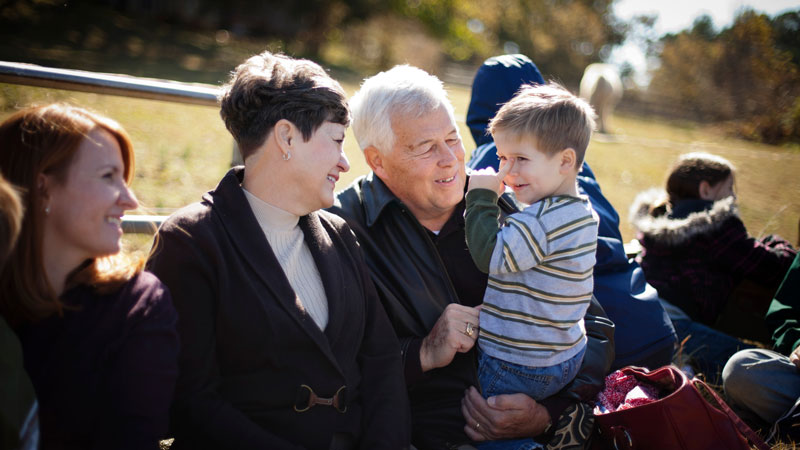 Grandparents with their kids and grandkids outdoors on a sunny day.