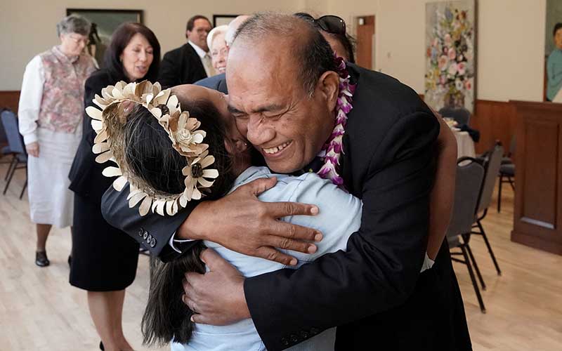 A Micronesian man wearing a suit woman hugging a Micronesian woman.