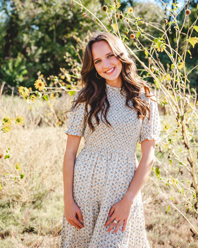 Morgan Hoyt standing in a sunny field with a few sunflowers behind her