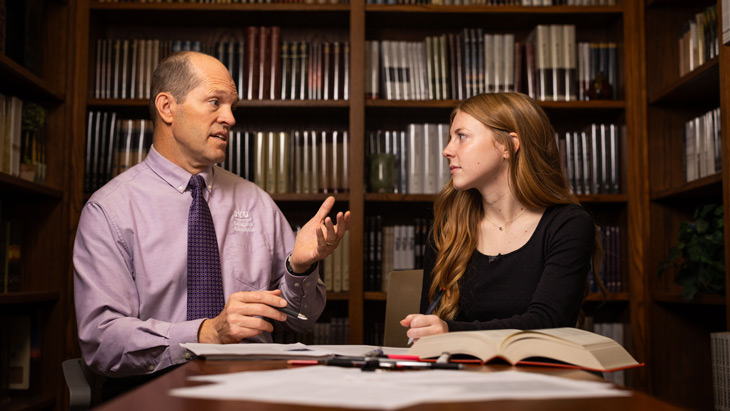 BYU student Emma Clark sitting in a library at a table learning from Executive Editor Devan Jensen