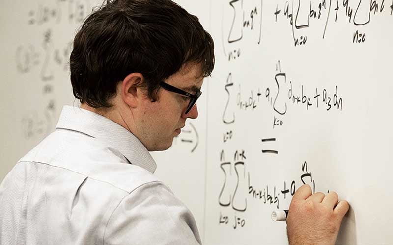 Jonathan Hales writes mathematical formulas on a whiteboard.