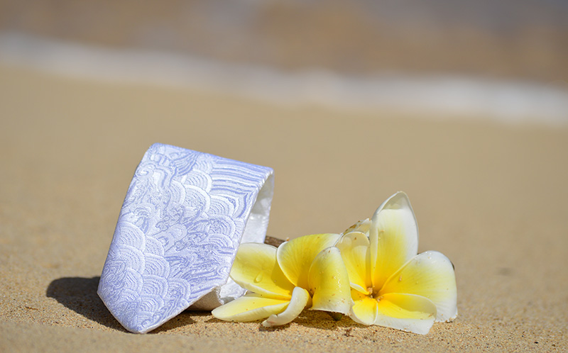 A white tie and a flower sitting on the sand.