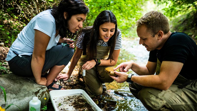 Male BYU religion professor and two female students studying a stream outdoors.
