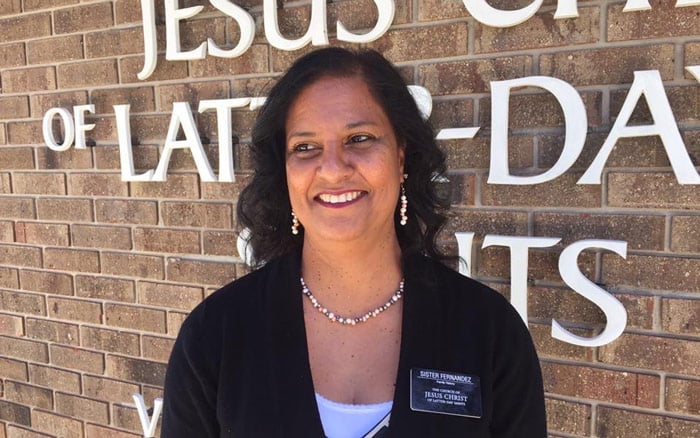 Yasmin Fernandez in front of a Latter-day Saint meetinghouse with a missionary tag.