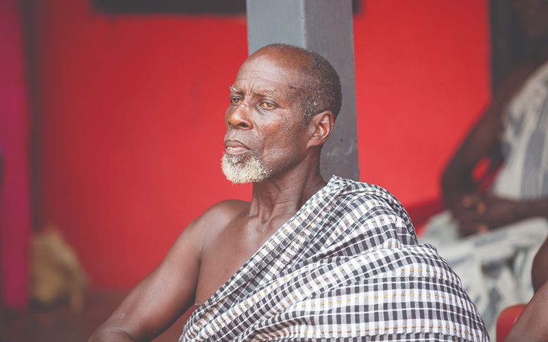 Photo taken in a village in Africa shows an elderly man with. colorful robe draping one arm. He is looking into the distance.