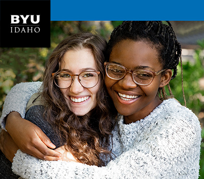 Two female BYU-Idaho students hugging and smiling at the camera. The BYU-Idaho logo is in the top left corner.