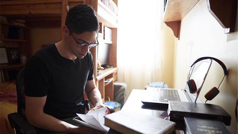A male BYU-Pathway student studying at a desk in his room.