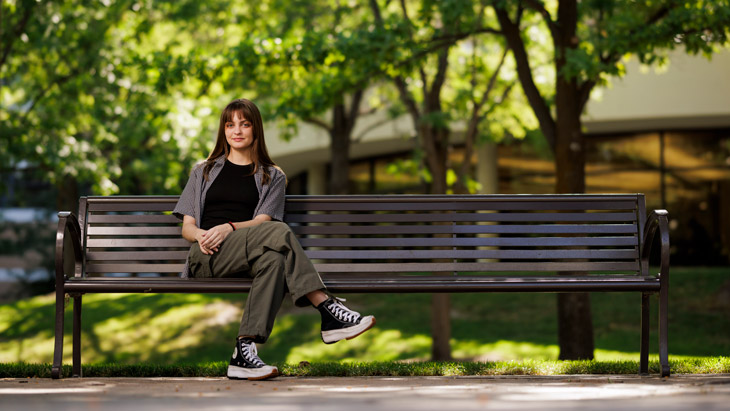 A female student sits on a park bench.