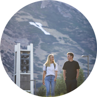 Two BYU students walking on campus with the bell tower and Y mountain in the background