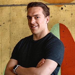 Portrait of a smiling BYU student wearing a black T-shirt with a painted concrete background.
