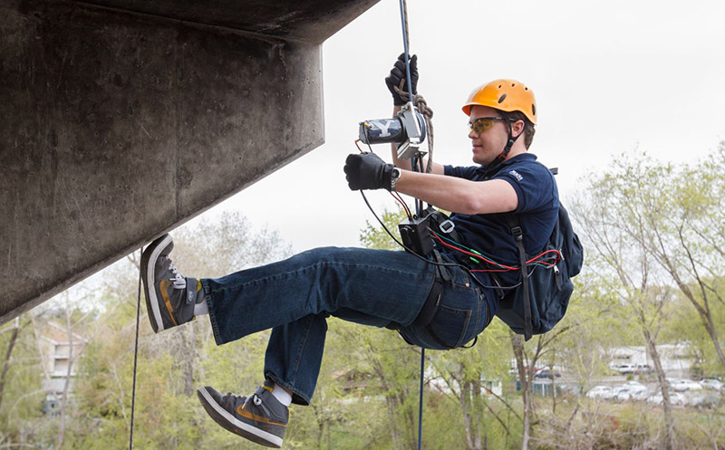 Student hanging in a harness with a camera inspecting a bridge