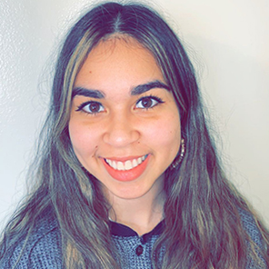 Portrait of a smiling BYU student with long gold and black ombre hair and a blue Henley shirt.